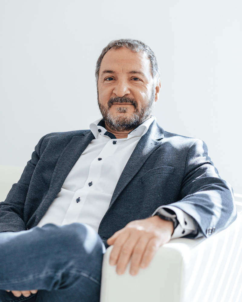 Alexandros Lagaris, Geschäftsführer von Laser Add Concept, sitzt auf der Couch, trägt Hemd und Sakko und blickt freundlich in die Kamera