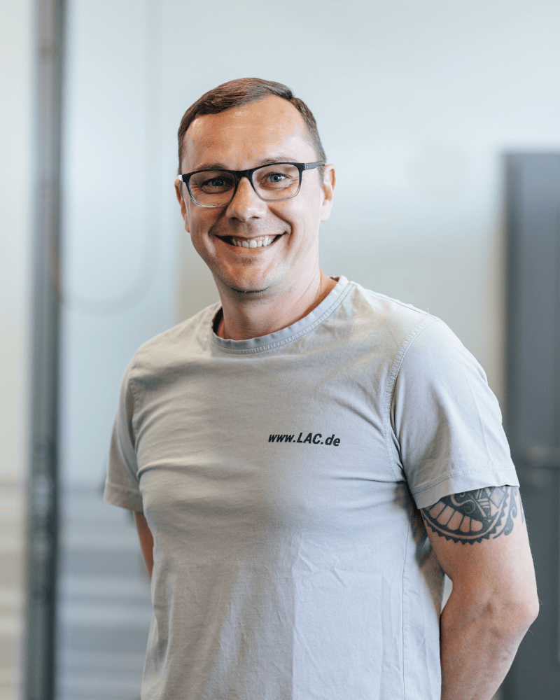 Ein Produktionsmitarbeiter von Laser Add Concept steht in der Produktionshalle, trägt Arbeitskleidung und hält die Hände locker hinter dem Rücken