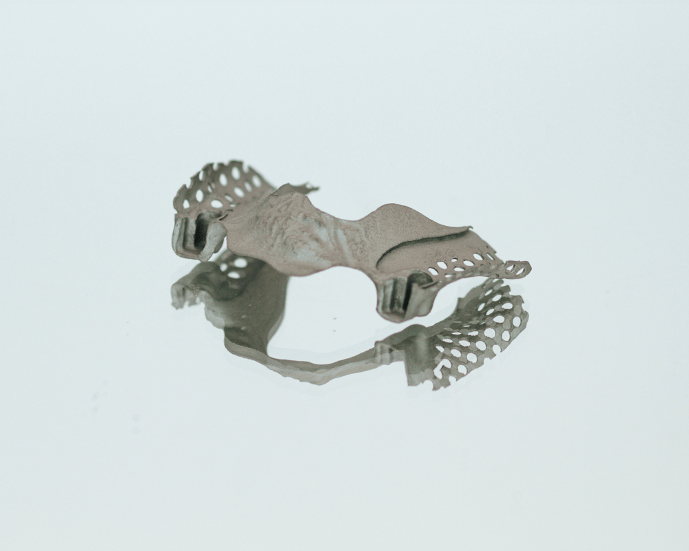 Ein Modellguss mit Stützstrukturen steht auf einem Spiegel vor neutralem Hintergrund und wurde im 3D Druck Service Metall gefertigt