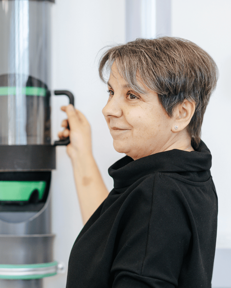 Eine Büro-Mitarbeiterin von Laser Add Concept steht an der Rohrpost, öffnet diese mit einer Hand und schaut lächelnd über die Schulter Richtung Kamera