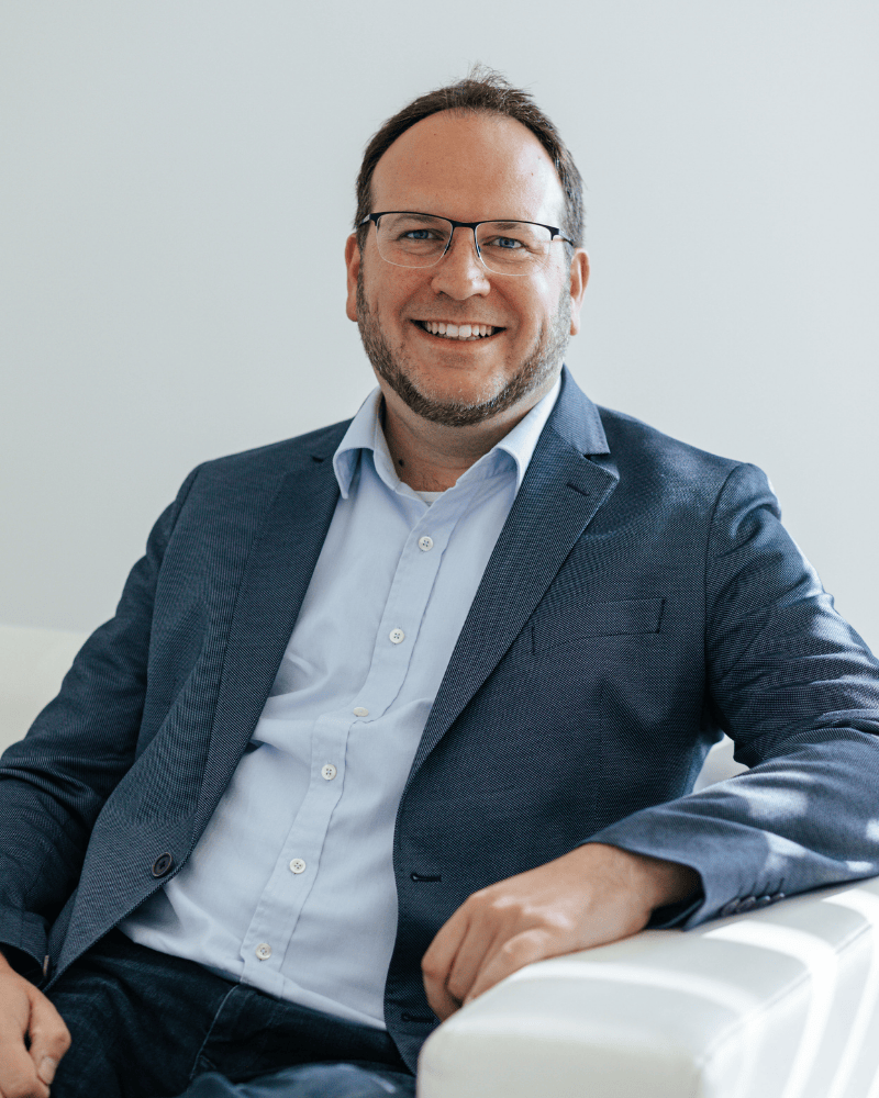 Rolf Ebert, Geschäftsführer von Laser Add Concept, sitzt auf der Couch, trägt Hemd und Sakko und lächelt mit locker abgelegtem Arm in die Kamera