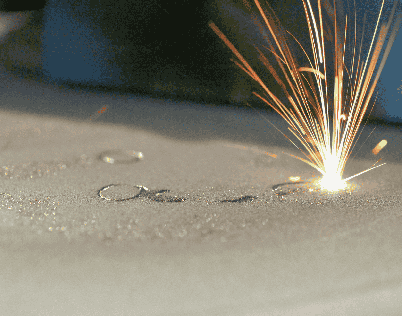Eine Nahaufnahme zeigt die Bauplatte in der SLM Maschine, auf der der Laser Metallpulver aufschmilzt und dabei sichtbare Funken erzeugt