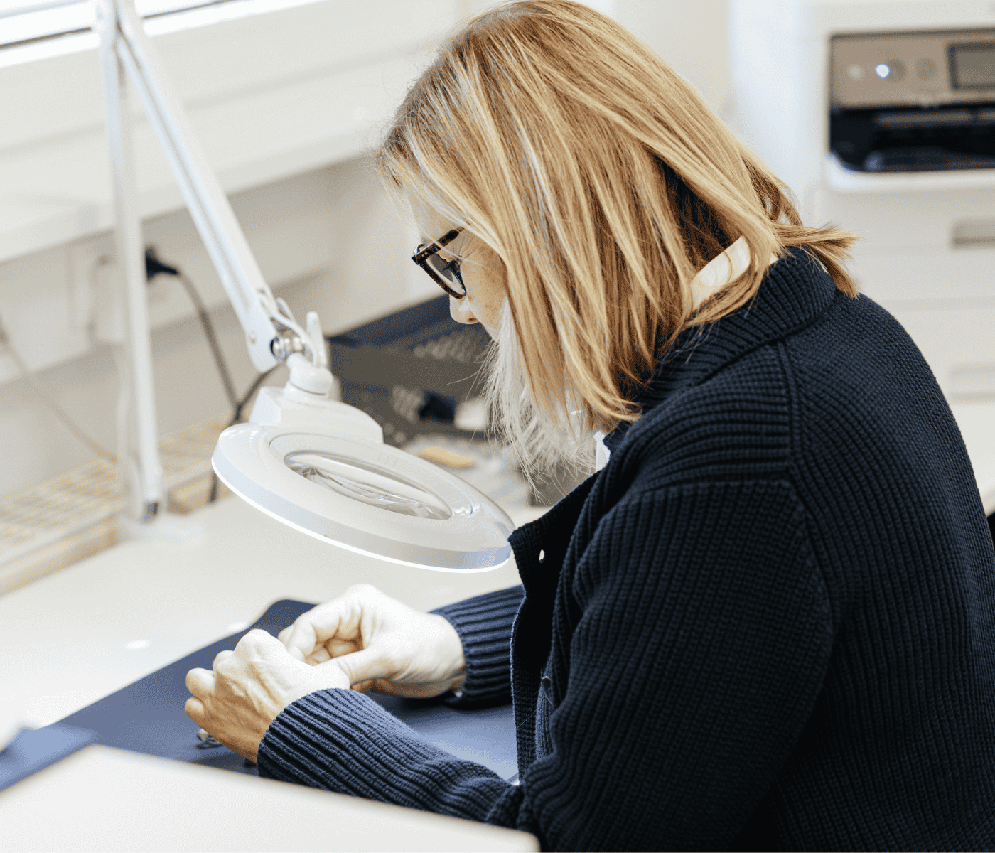 Eine Mitarbeiterin von Laser Add Concept hält ein Wirbelsäulenimplantat aus Titan mit beiden Händen unter eine Lupe zur Sichtprüfung