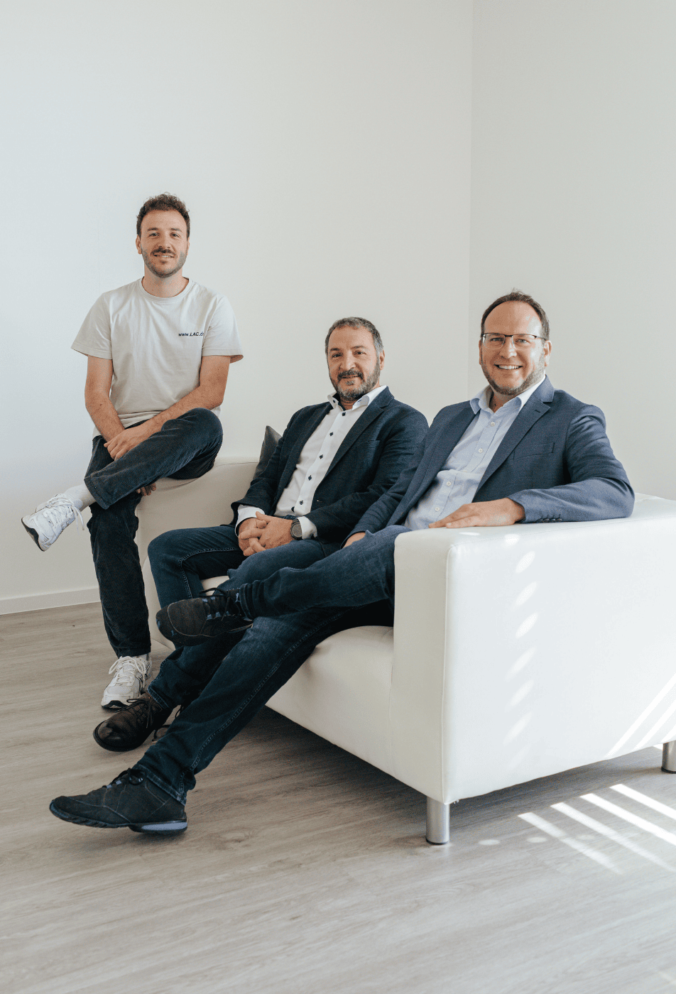 Drei Mitarbeitende von Laser Add Concept sitzen und stehen im Büro und schauen in die Kamera beim Teamfoto für den 3D Druck Dienstleister