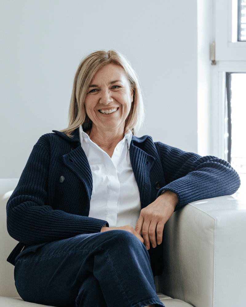 Eine Büro-Mitarbeiterin von Laser Add Concept sitzt entspannt auf einer Couch, hat die Beine übereinander geschlagen und lächelt in die Kamera
