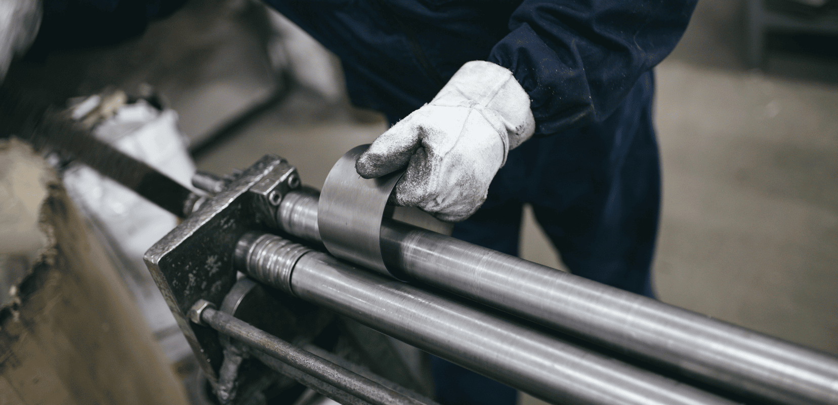 Eine behandschuhte Hand hält ein Metallstück, das in einer Maschine eingespannt ist und dort gebogen wird