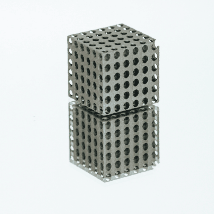 Ein vom SLM Dienstleiter Laser Add Concept gefertigter löchriger Metallwürfel, der auf einem Spiegel steht.